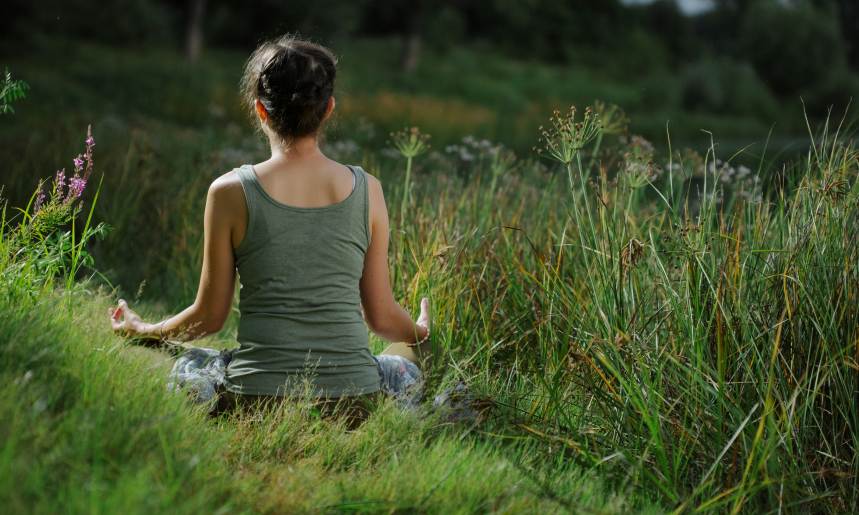 Woman doing meditation and relax at blooming spring lush meadow with green grass. back view
