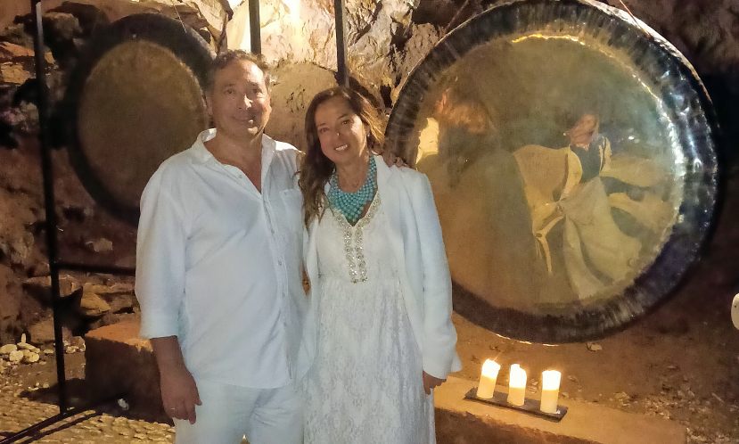 Elena y José Carlos vestidos de blanco tocando los gongs en la Gruta de las Maravillas, símbolo del apoyo integral y la experiencia que ofrece la Hospedería de la Corte a los organizadores de retiros.